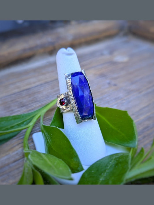 Handcrafted Lapis Epoch Ring by K. Elizabeth Jewelry featuring a rectangular lapis lazuli stone with a small garnet accent on a textured silver adjustable band inspired by tree bark.