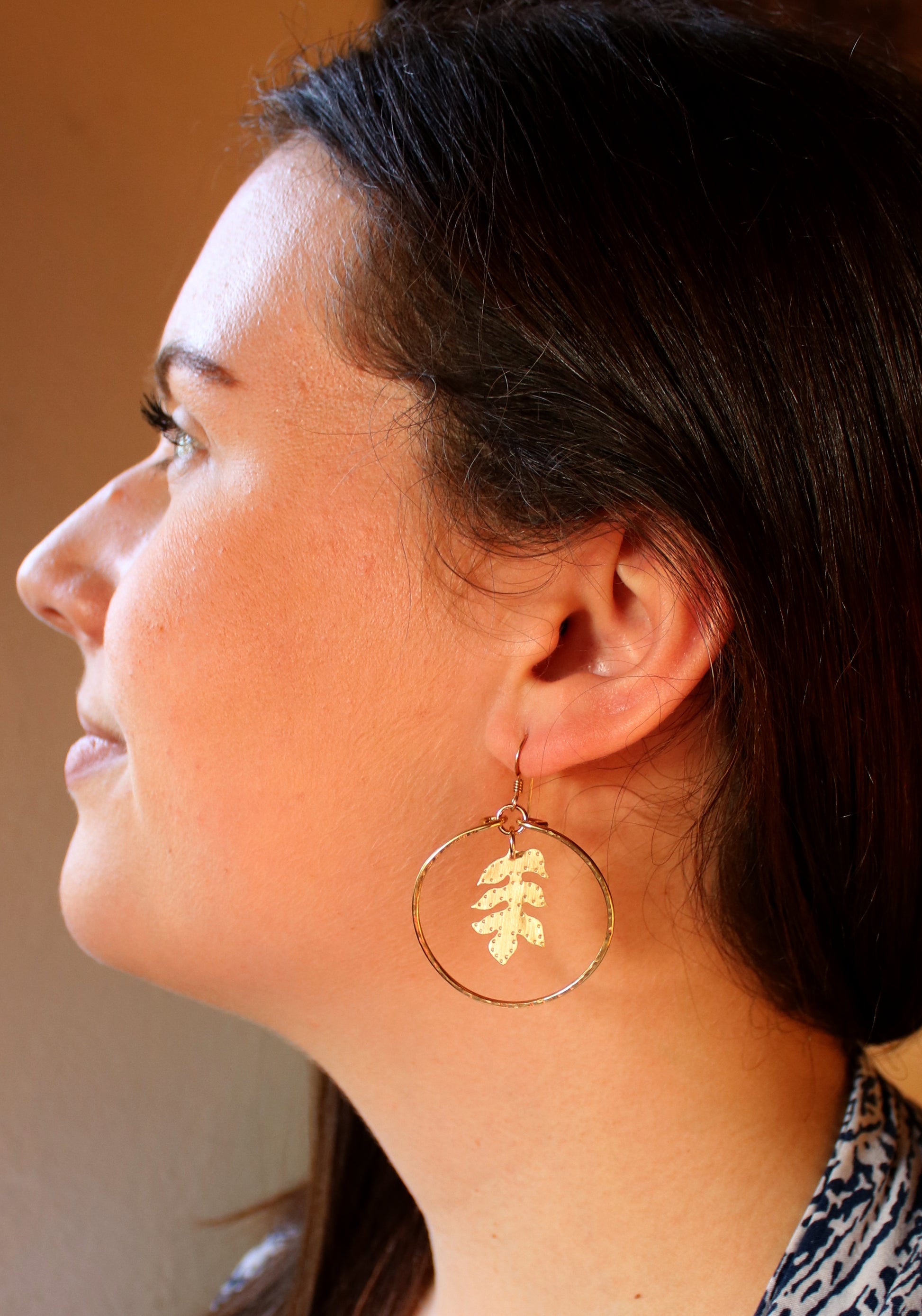 Woman wearing handcrafted brass sassafras hoops, earthy bohemian jewelry inspired by nature and grounded elegance.